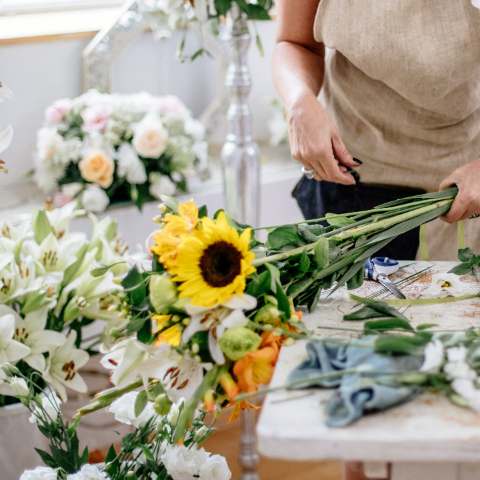 Florista montando um arranjo com girassóis e flores brancas